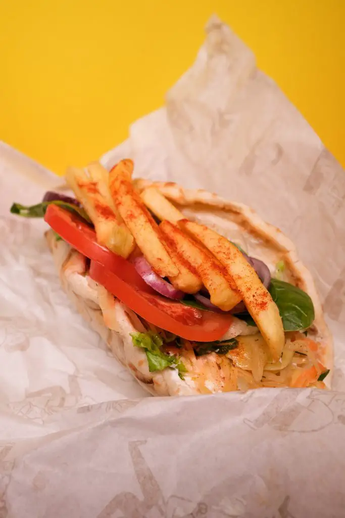 gyros wrap with fries and salad on orange background